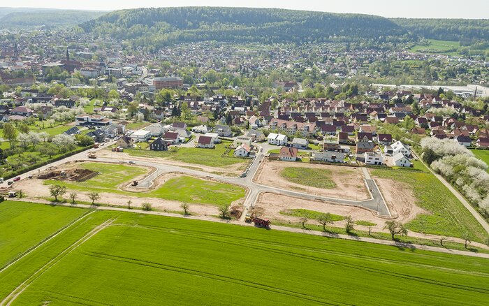 Luftaufnahme eines im Bau befindlichen Wohngebiets mit angrenzenden Feldern und Einfamilienhäusern.