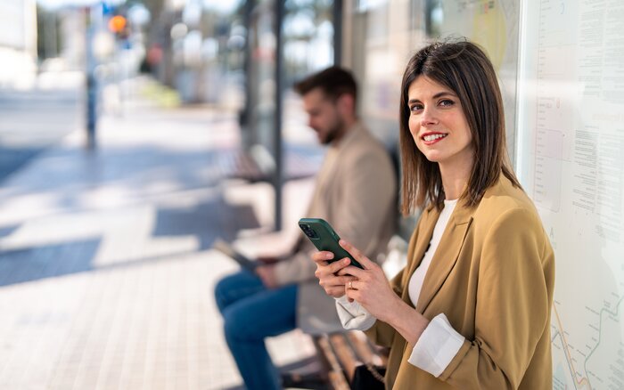 Zwei Personen an Bushaltestelle mit Smartphone und Tablet