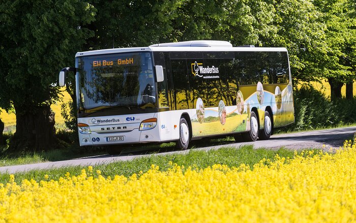 Bus mit Aufschrift „WanderBus“ fährt durch grüne Landschaft
