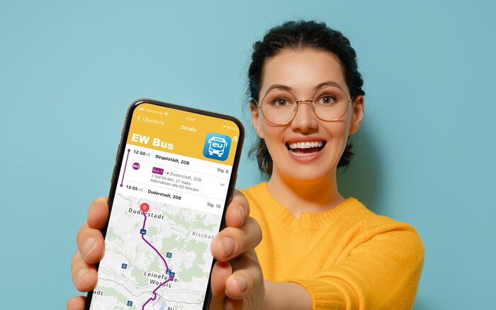 Person mit gelbem Pullover hält Smartphone mit Busroute „EW Bus“ auf dem Bildschirm.