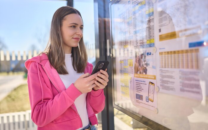 eine Person an Bushaltestelle mit Smartphone