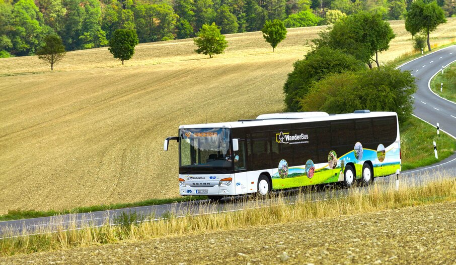 Der WanderBus der EW Bus fährt bei Kalteneber auf einer Landstraße im Sommer. Man sieht Wald und Felder. 