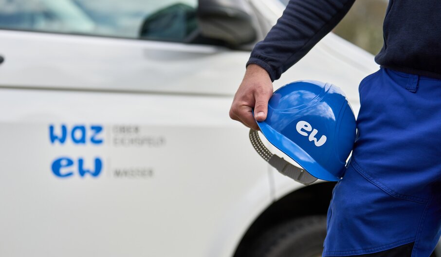 Mitarbeiter der EW Wasser mit Helm in der Hand vor einem Betriebsauto.