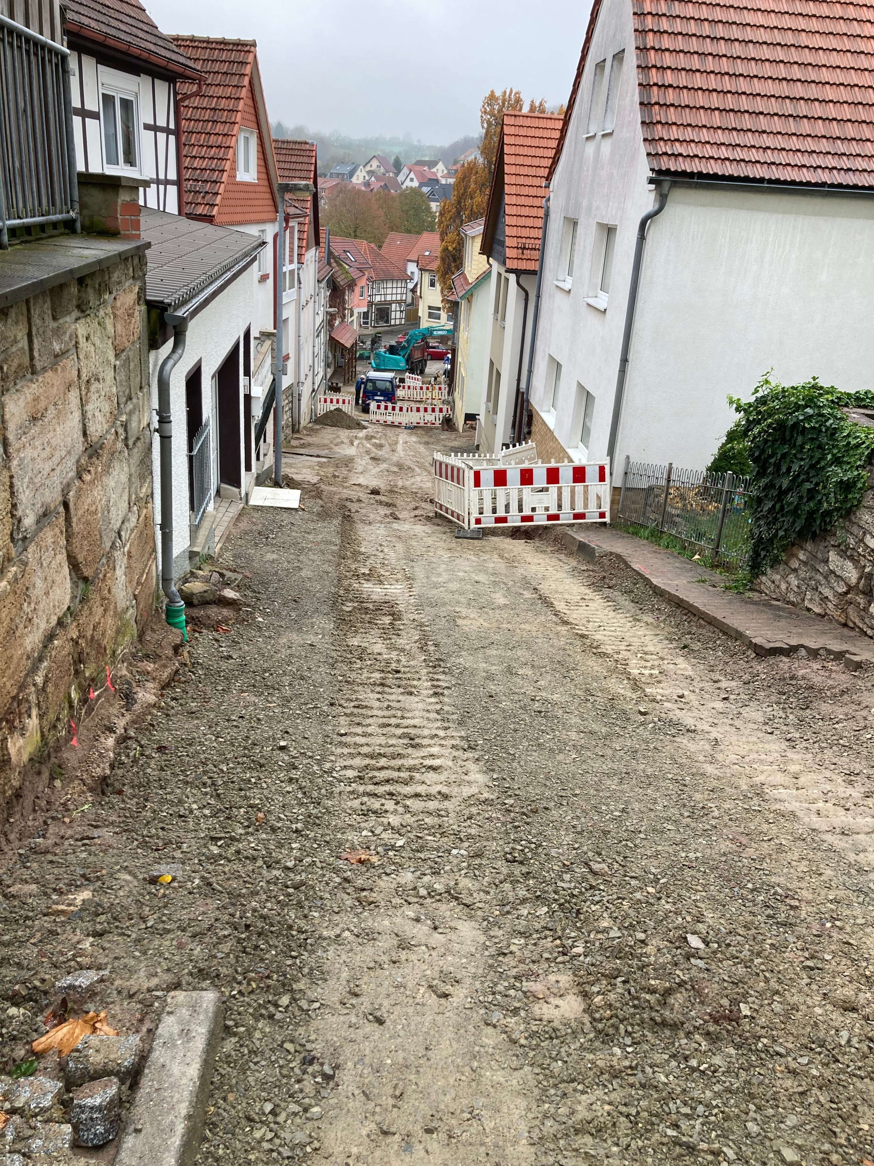 Eine Straße mit Schotterschicht und Baustellenschilder am Rand.