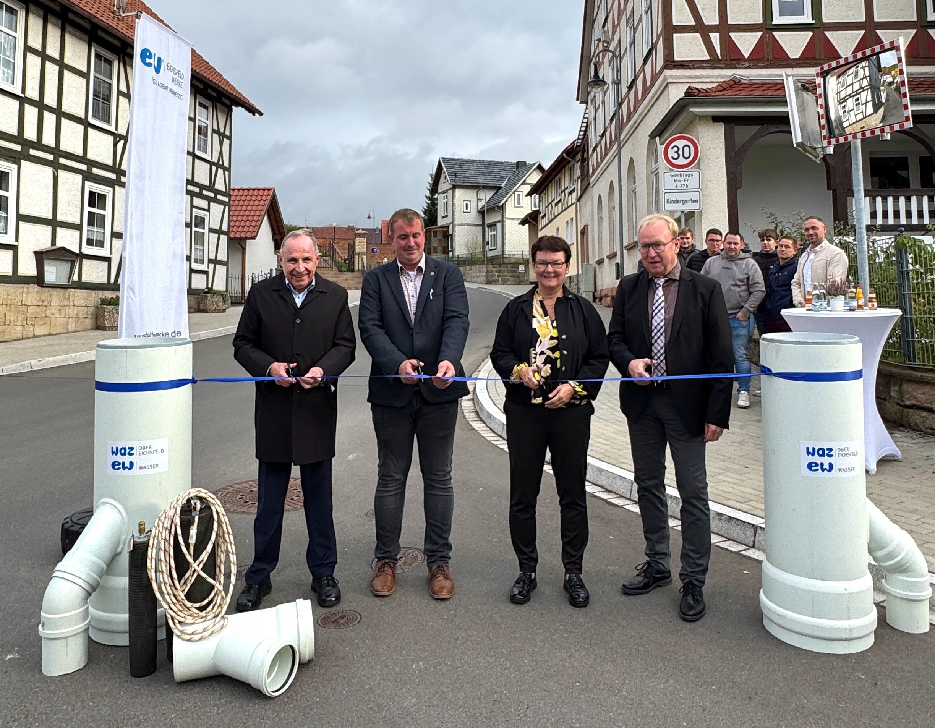 Eröffnung der Ortsdurchfahrt in Lutter: Zum Abschluss des ersten Bauabschnitts in Lutter im Oktober 2025 gaben (v. l.) EW-Geschäftsführer Ulrich Gabel, Ortsbürgermeister Christian Werner, Landrätin Dr. Marion Frant und Adrian Grieß, Verbandsvorsitzender des WAZ Obereichsfeld, die Ortsdurchfahrt offiziell frei. Das Band wurde von Rohrleitungen links und rechts gerahmt und veranschaulichte, was zu diesem Zeitpunkt bereits unter der Straße verlegt worden war.
